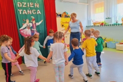 Dzieci stoją w parach twarzami do siebie trzymając się za ręce. Za nimi dekoracja z płótna oraz napis Dzień  Tańca.