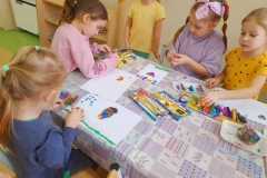 Cztery dziewczynki siedzą przy stoliku, wyklejają tęczę z plasteliny.