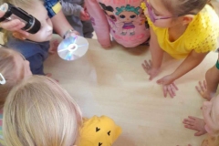 Dzieci zgromadzone wokół stolika przy którym pani świeci latarką na płytkę CD, powstaje tęcza.