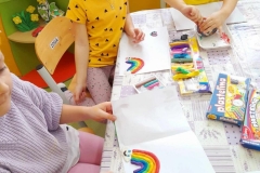 Trzy dziewczynki siedzą przy stoliku, wyklejają tęczę plasteliną.