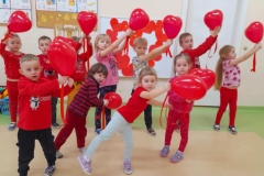 Dzieci ubrane na czerwono tańczą do muzyki z czerwonymi balonami.