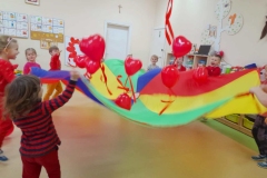 Dzieci podrzucają w rytm muzyki czerwone balony na chuście animacyjnej.