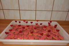 W białym prostokątnym pojemniku leżą ciasteczka w kształcie serduszek.  Każde z nim polane jest czerwonym lukrem.