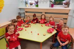 Pięcioro dzieci siedzi przy  stoliku i maluje różowe i czerwone serduszka.
