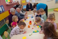 Dzieci wraz z seniorami siedzą przy stolikach, wykonują laurki dla babci I dziadka.