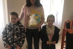 Zdjęcie przedstawia trzy osoby, kobietę i dwoje dzieci  - dziewczynkę i chłopca. Kobieta trzyma w ręce stroik świąteczny.