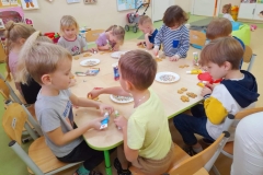 Dzieci siedzą przy stolikach, dekorują pierniczki.