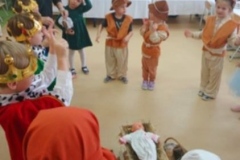 Dzieci przebrane za postacie z jaselek tańczą w kole, w tle siedzą zaproszeni goście.