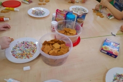 Na stole leżą ciasteczka i posypki do dekoracji ciasteczek.