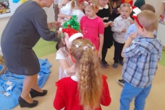 Wychowawczyni łamie się opłatkiem z dziećmi, w tle choinka.