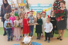 Na zdjęciu dzieci z wychowawczynią, przed nimi żłobek, czworo z nich trzyma w ręku stroiki.