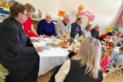 Przy stolikach siedzą Seniorzy, ksiądz.