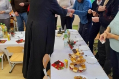 Seniorzy łamią się opłatkiem z księdzem.