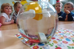 Na kolorowej serwetce szklana kula z wodą , a w niej zanurzone różne przedmioty .niektóre z nich utrzymują się na powierzchni wody , niektóre toną.