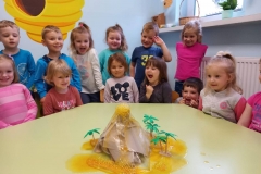 Dzieci zgromadzone przy zielonym stoliku obserwują wypływającą żółtą lawę, która rozlewa się po blacie stolika. Na twarzach dzieci widać radość i uśmiech.