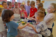 Kilkoro dzieci stoi wokół stołu, na stole leży ziemia  doniczki, torebki z nasionami warzyw.