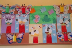 Na tablicy wiszą wiosenne prace: kolorowe motyle oraz bociany wycięte z płatków kosmetycznych, bociany siedzą na czerwonym kominie.