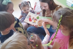 Kilkoro dzieci siedzi wokół pani, oglądają książki.