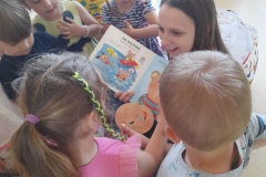 Kilkoro dzieci siedzi wokół pani z biblioteki, dopasowują minki do zachowań misia.