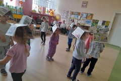 Dzieci chodzą z gazeta na głowie w rytm muzyki. Starają się by gazeta nie spadła z głowy.