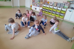 Wiesława Patoń Dzieci siedzą na podłodze Na gazetach, przesuwają się na nich do przodu i do tył. W tle widać kolorowe piłeczki dzieci.