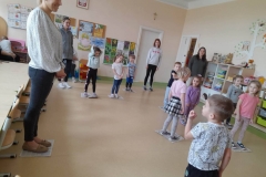 Dzieci oraz czworo rodziców stoją na gazetach słuchają muzyki, na stopach w muzyce zmieniają miejsca.