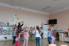 Grupa dzieci stoi w kole, wykonuje ruchy do słów piosenki. Dzieci podnoszą ręce do góry.