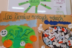 Wiesława Patoń Na tablicy ilustracje dotyczące Dnia Ziemi. Pod tablicą plakat przedstawiający kolorową, wesołą Ziemię  i smutną  czarna Ziemię.