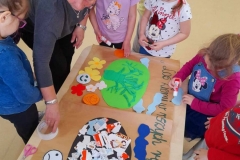 Kilka dziewczynek naklejają na smutną i wesołą Ziemię różne elementy. Wychowawczyni pomaga im.