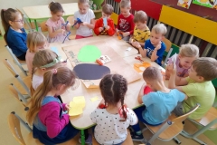 Grupa dzieci siedzi wokół stolików, wycinają różne elementy potrzebne do plakatu. Na stoliku leżą zielona i czarna kartka w kształcie Ziemi.