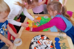 Dzieci zgromadzone wokół plakatu, naklejają różne elementy na wesołą i smutną Ziemię.