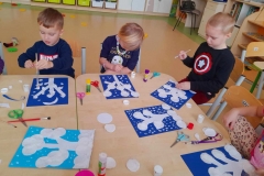 Trójka dzieci wykonuje zimowy krajobraz na granatowej kartce.