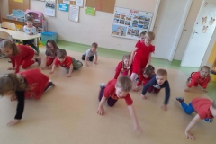 Dzieci ubrane na czerwono chodzą na czworakach naśladując pieski do muzyki.