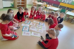 Dzieci siedzą w półkolu na podłodze, między nimi rozłożone obrazki, dzieci opowiadają co się na nich dzieje.