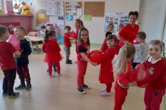 Dzieci wraz z wychowawczynią ubrane na czerwono, tańczą w parach do muzyki trzymając   między sobą czerwony balon.
