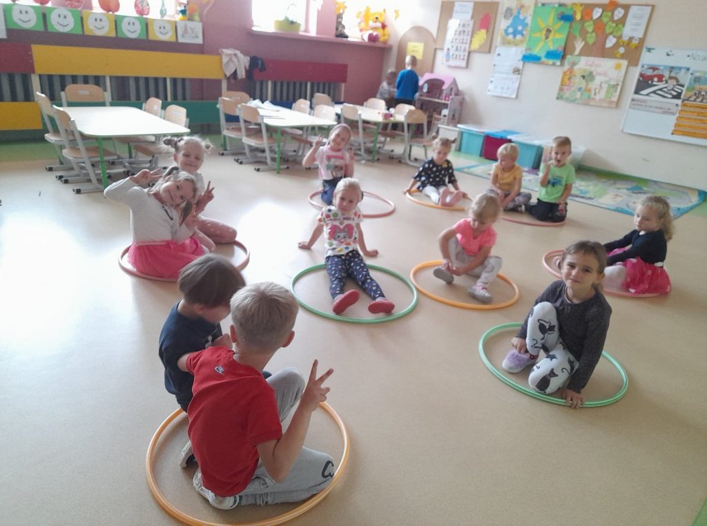 Dzieci siedzą w hula hopach wykonując różne ćwiczenia.