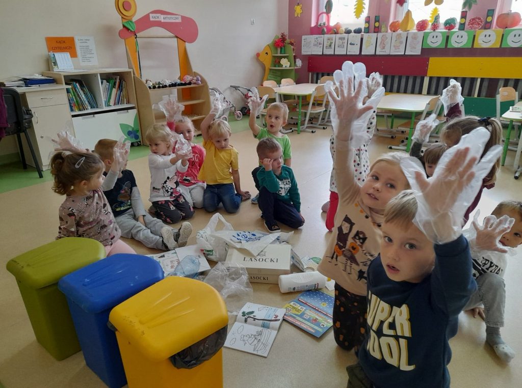 Dzieci siedzą w kole zakładają foliowe rękawiczki aby posegregować odpady 